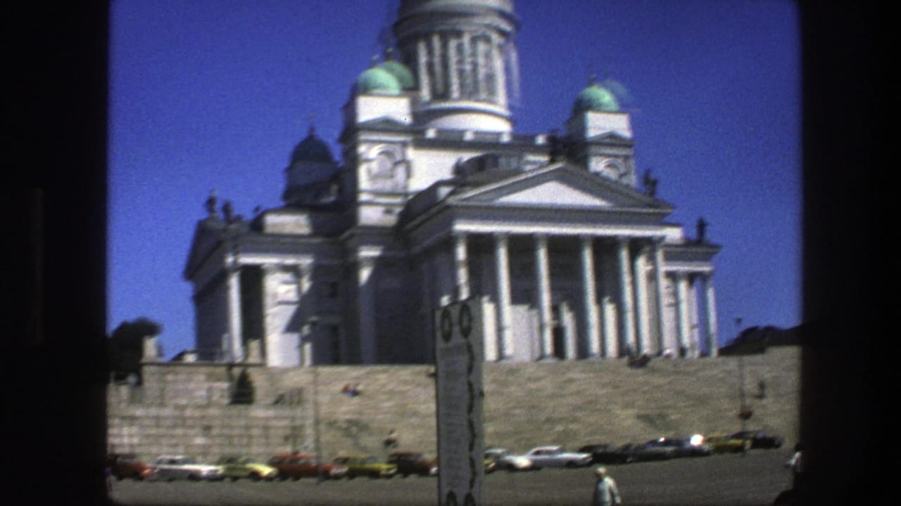 Cathedral facade and domes with a signboard, parked cars, and people near the steps.
