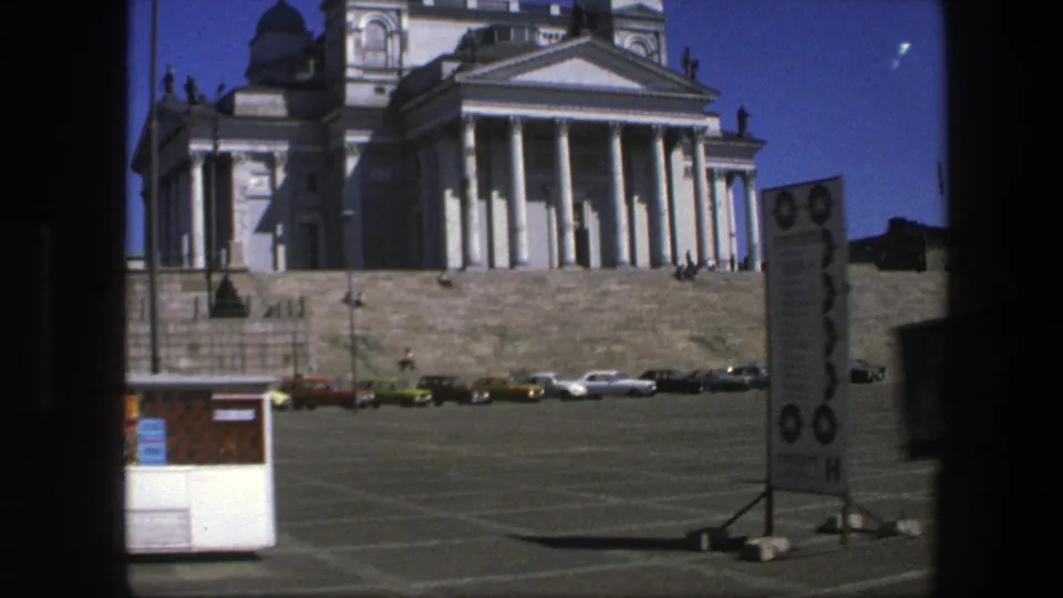 1975 Sweden 8mm frame with cathedral columns and domes partly cropped, broad steps, parked cars, a signboard, and a small kiosk in the square.
