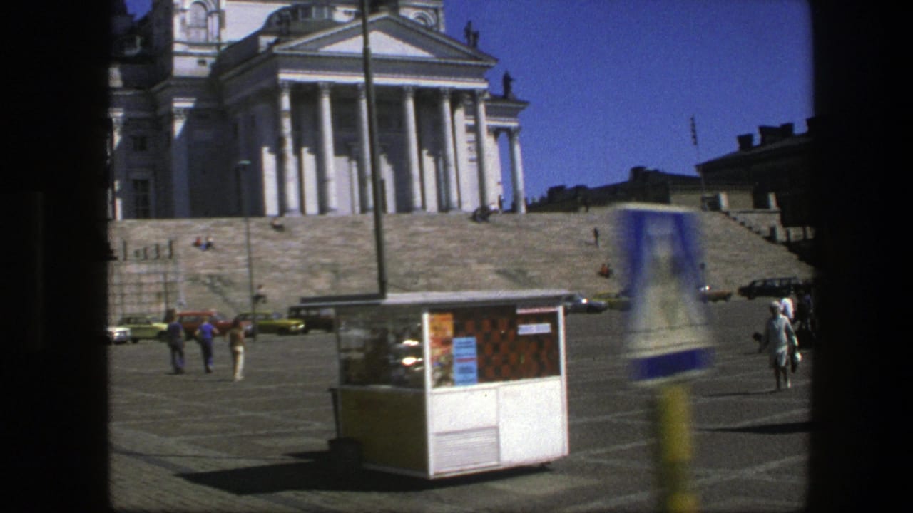 Public square with a white columned building, kiosk, pedestrians, cars, and dark frame edges.