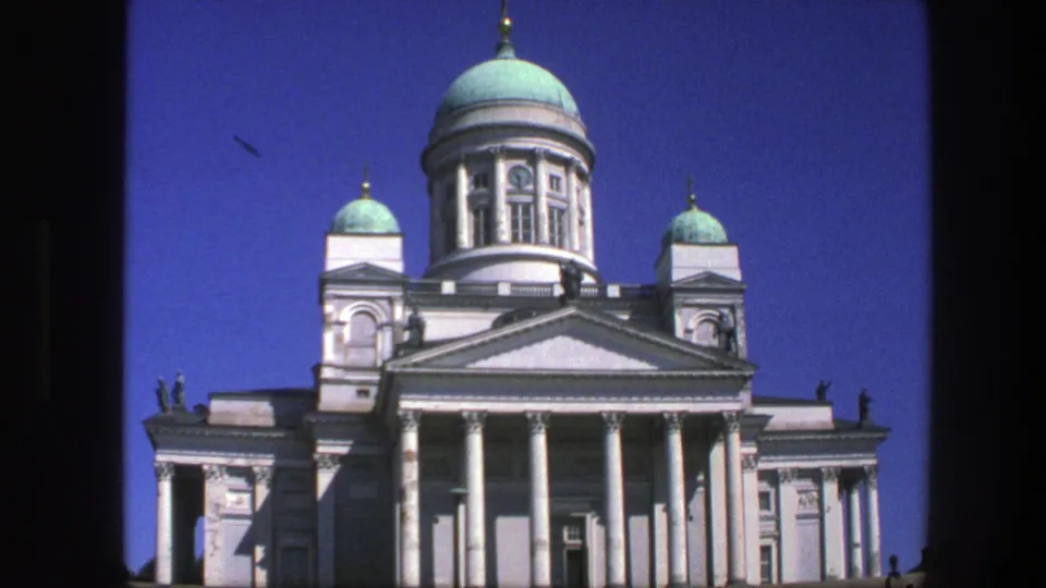 Close 1975 8mm view of a white neoclassical domed landmark with columns and turquoise domes under clear blue sky.