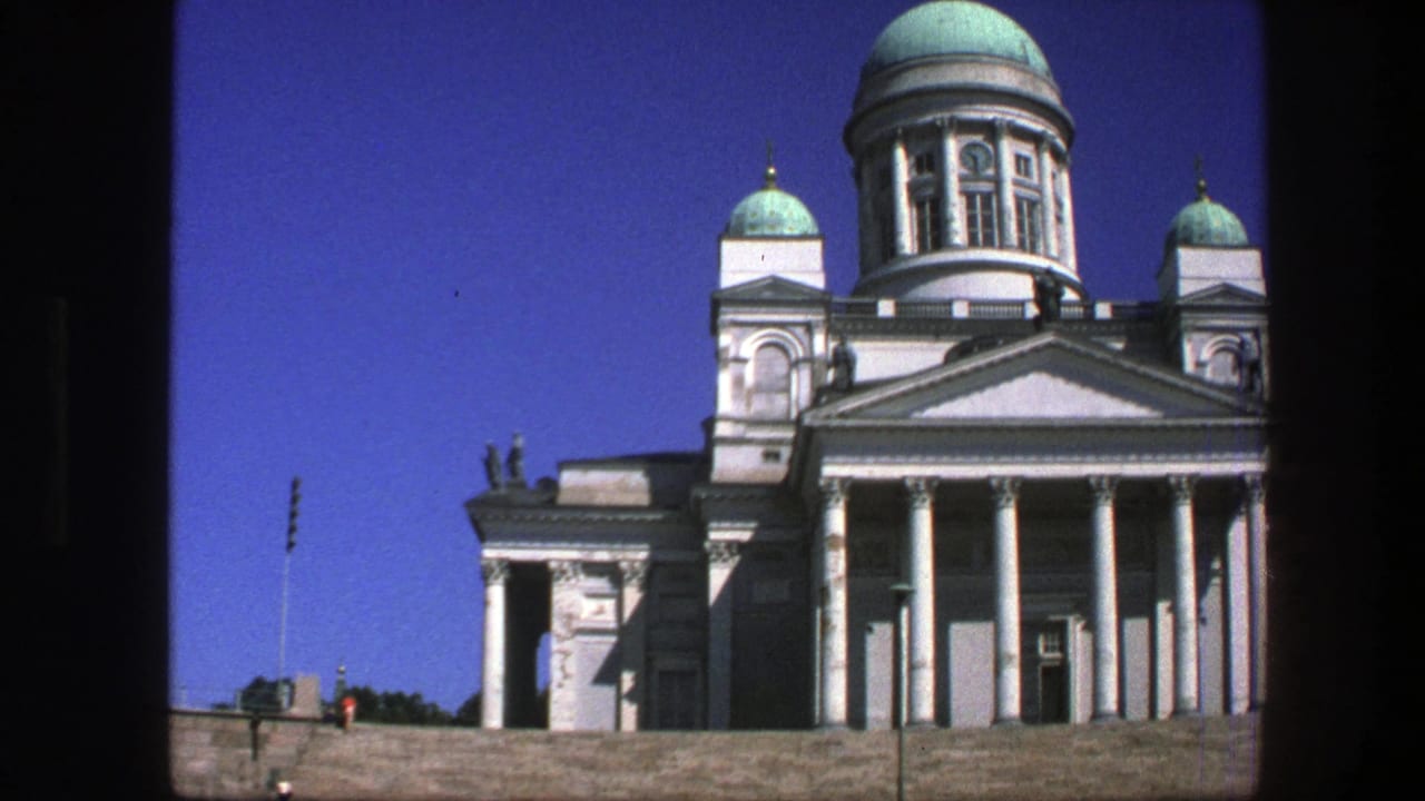 1970s 8mm view of Helsinki Cathedral with white columns, green domes, stone steps, and small visitors in the distance.
