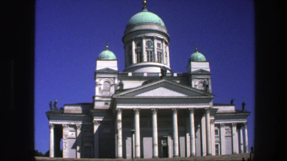 Closer 8mm frame of Helsinki Cathedral's central dome, white colonnade, pediment, and flanking towers under clear daylight.