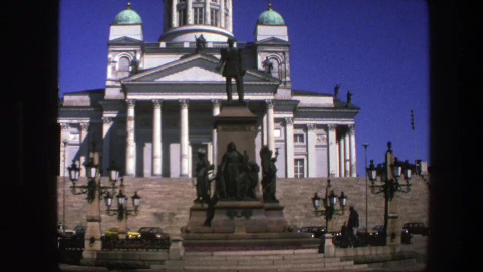 Cataloged 1975 travel footage shows the domed facade behind a public monument, lamps, cars, and small pedestrians.