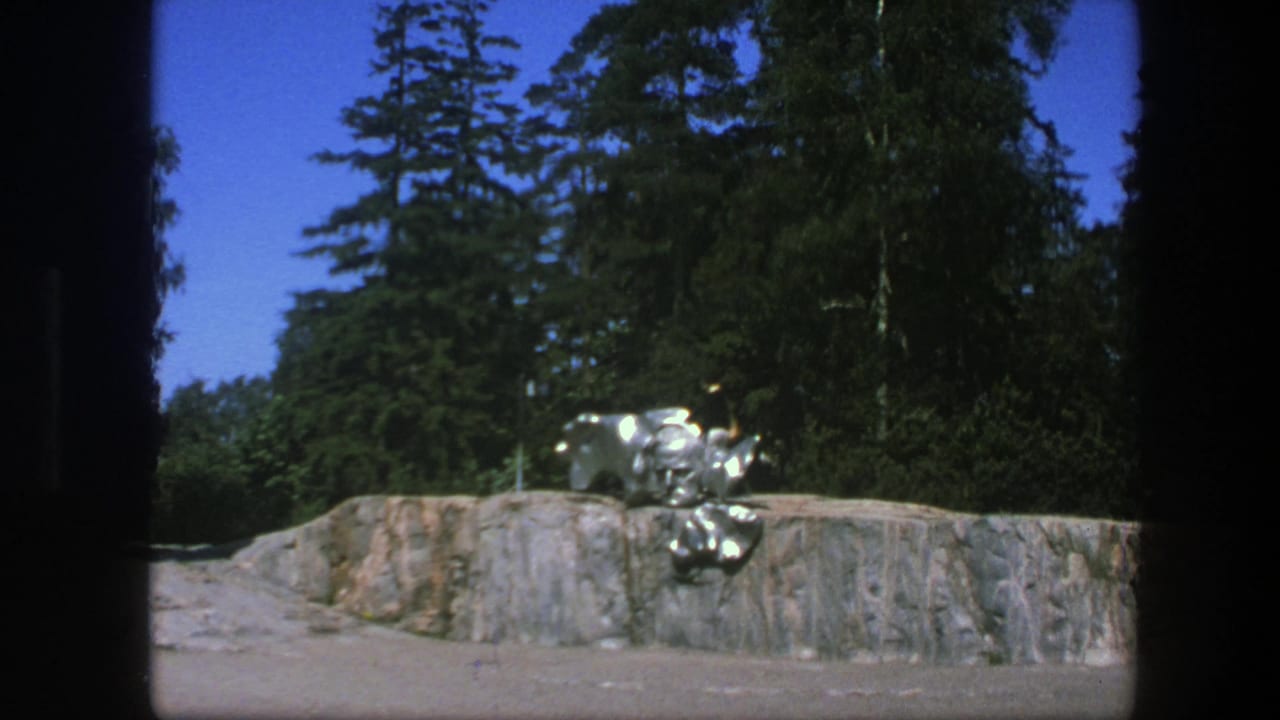 Silver sculpture on a stone platform with tall trees behind it.