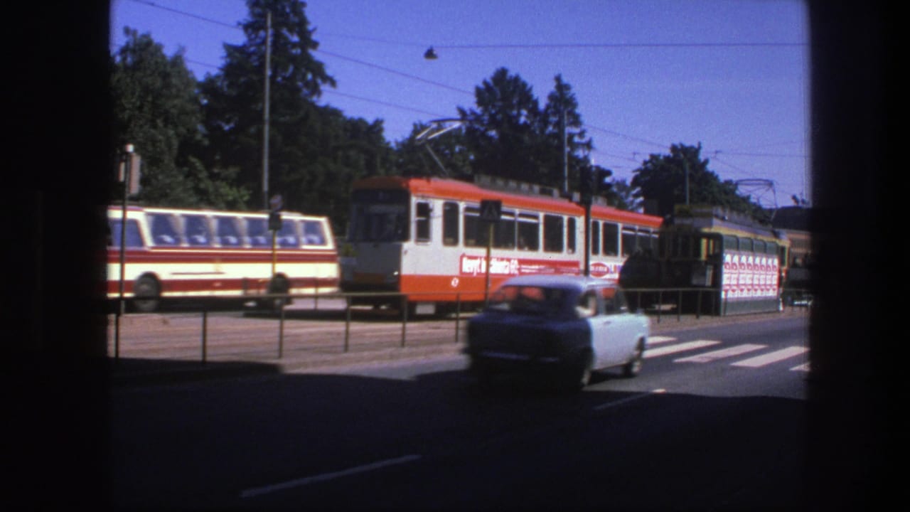 Orange-and-white electric tram stopped near a crosswalk as a light-colored car passes in front.