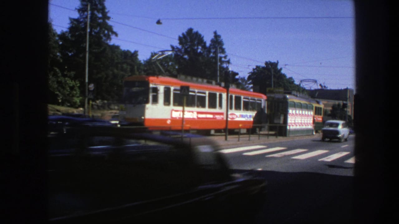 Electric tram and bus near a crosswalk, partly obscured by a dark passing car.