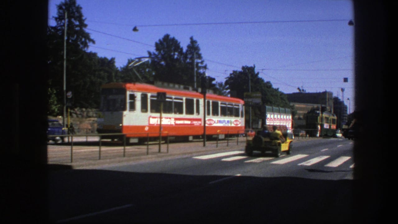 1975 Sweden 8mm view from inside a vehicle showing a red-and-white tram, zebra crossing, roadside railings, trees, and traffic.