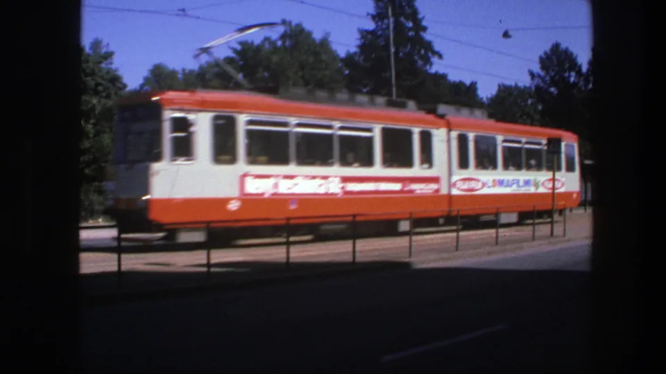 Close 8mm frame of a red-and-white tram with visible side advertising passing roadside railings in Sweden in 1975.