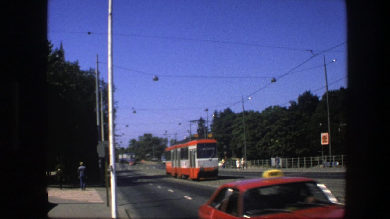 1975 Sweden avenue scene with a red-and-white trolley approaching and a red taxi crossing the foreground under overhead wires.