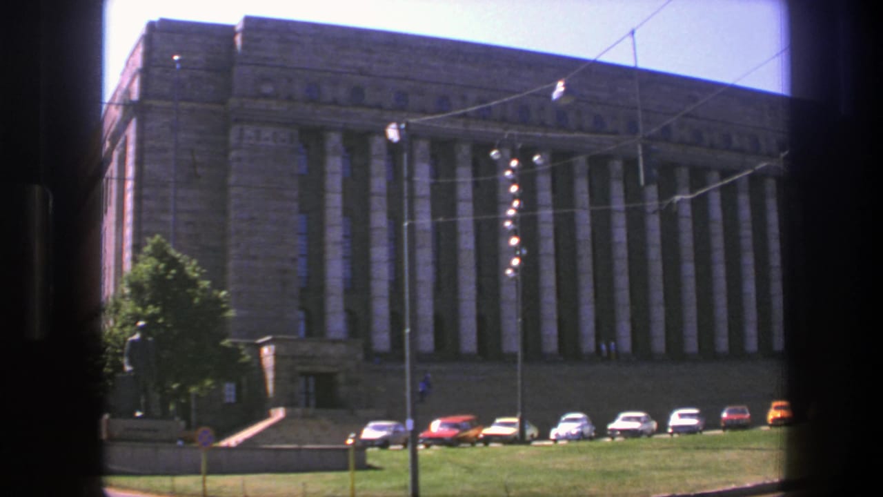 1975 Sweden frame of the civic hall exterior with its columned facade, parked cars along the base, lawn, wires, and street lighting.