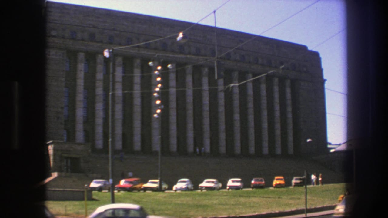 1975 Sweden street view of a large columned stone building, with vintage cars along the curb and overhead wires crossing the sky.
