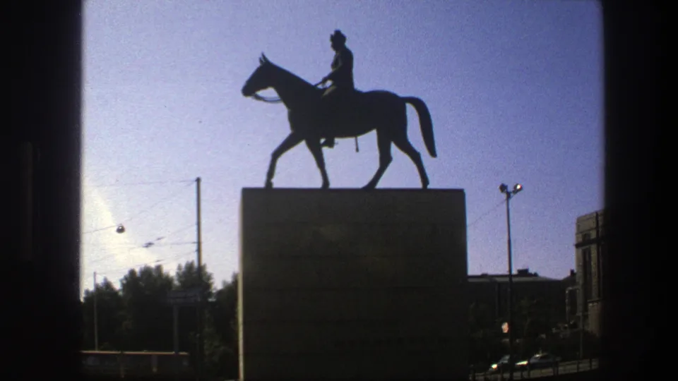 1975 Sweden 8mm frame showing an equestrian statue in silhouette above a stone pedestal, with street wires and buildings nearby.