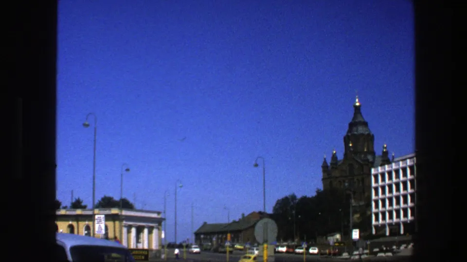 1975 Sweden urban street view with cars, road signs, lamp posts, low buildings, blue sky, and an ornate tower partly at the right.