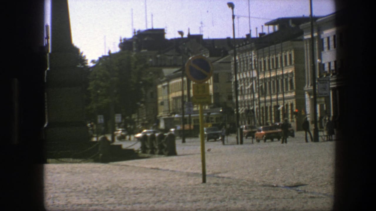 Cobblestone city street with pedestrians, cars, buildings, and a street sign.