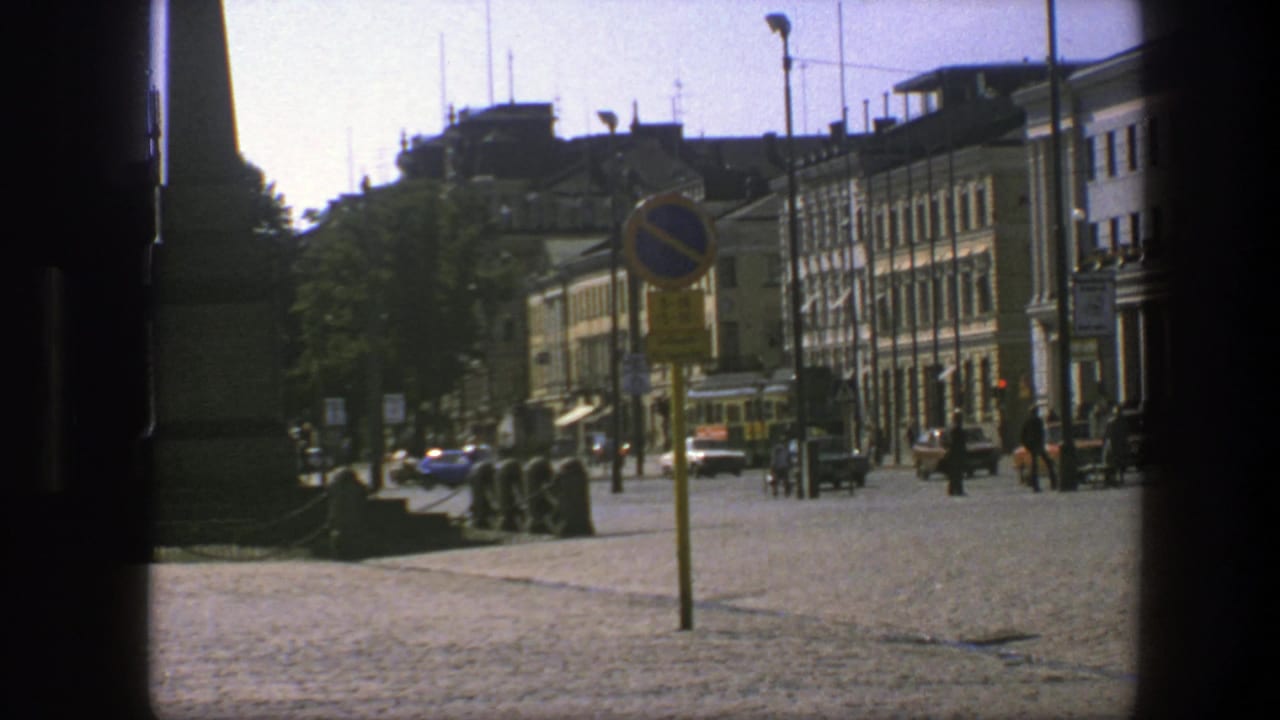 1975 Sweden urban street scene with compact cars, pedestrians, a cobblestone foreground, and rows of city buildings.