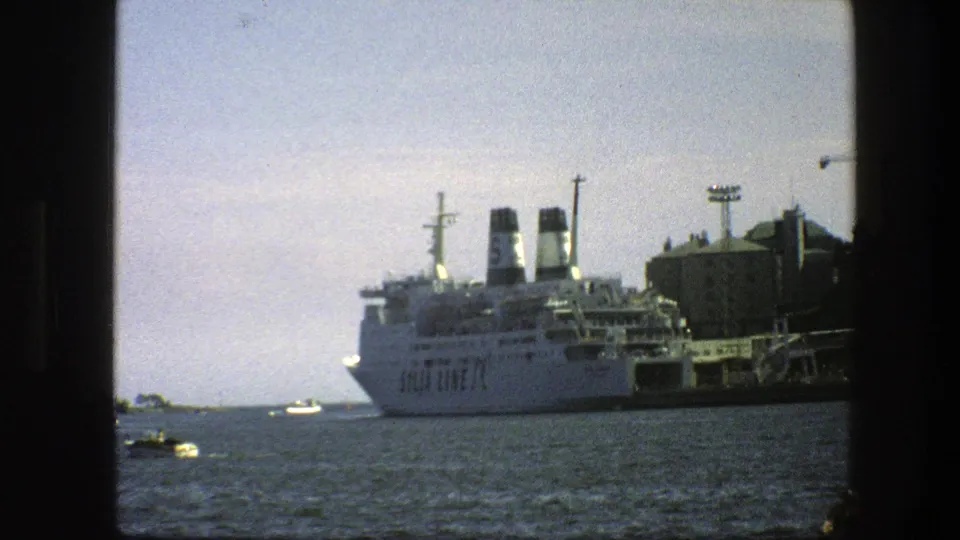1975 Sweden waterfront view with a large docked passenger ship, small boats crossing the water, and harbor buildings in the background.