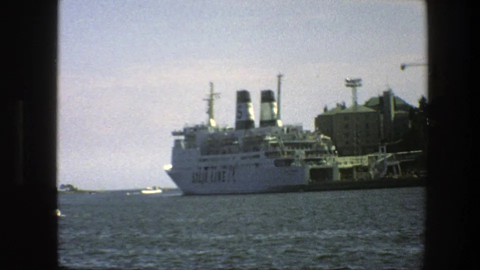 Large white passenger ferry at a Swedish harbor in 1975, with port buildings and water visible in the foreground.