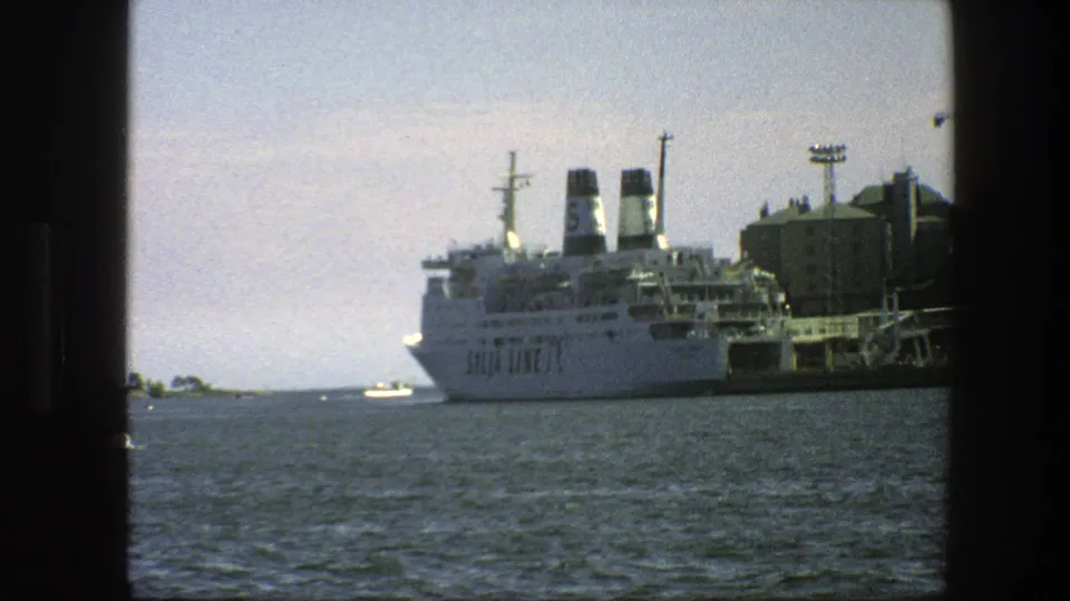 1975 harbor view with a large docked ferry, small boat, pier structures, and open water in Sweden.
