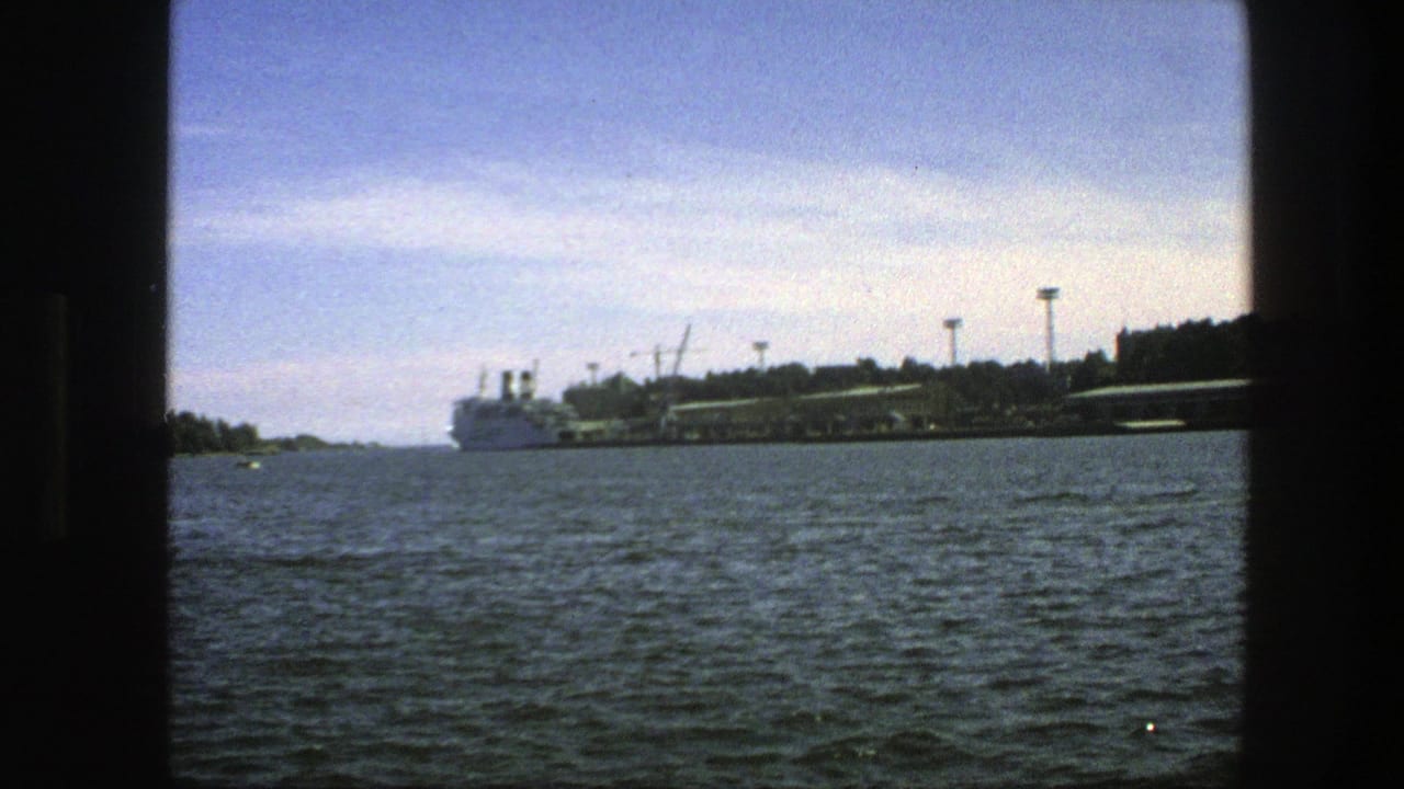 Waterfront seen across rippled water with a large white ship and dark window-frame edges.