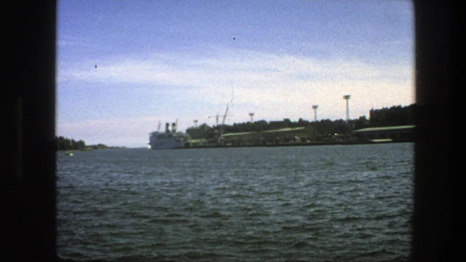 Swedish port view from 1975, showing a large white ship near the shore, waterfront structures, trees, and dark 8mm frame edges.
