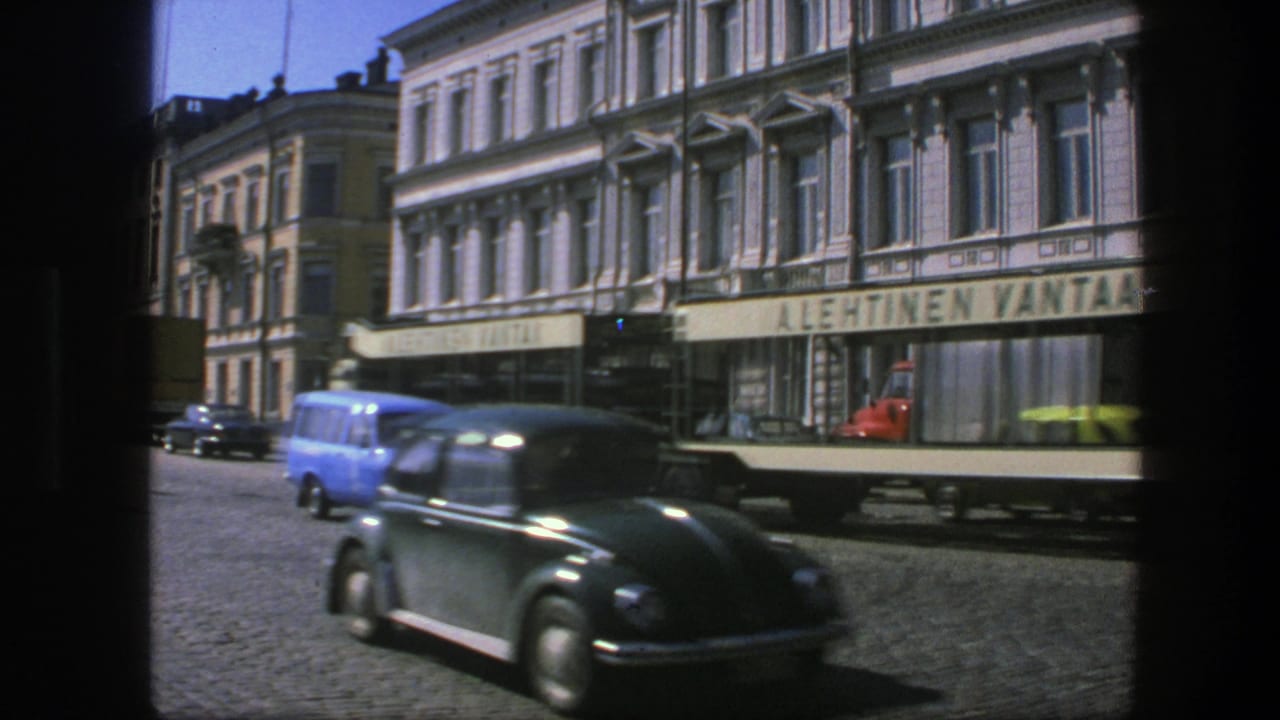 Streetcar and dark Volkswagen Beetle pass storefronts on a cobblestone city street.