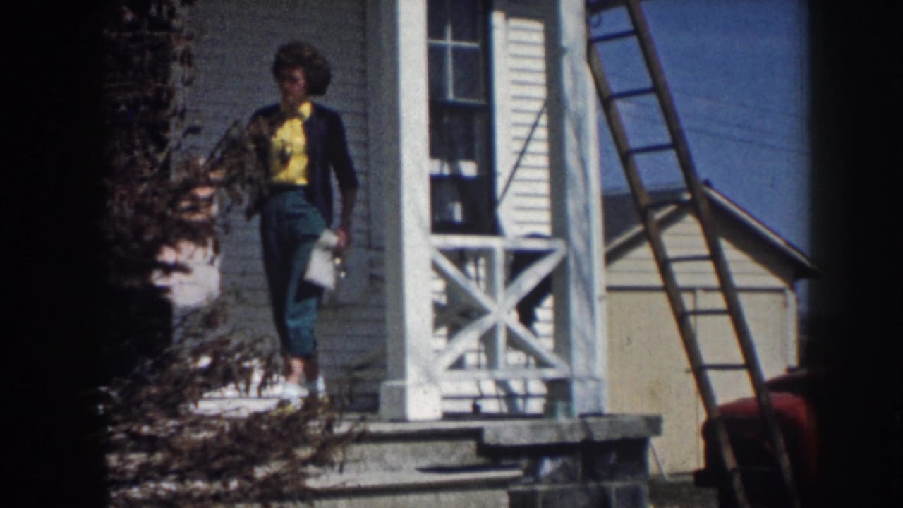 Woman in a yellow shirt stands on a porch holding a light garment.