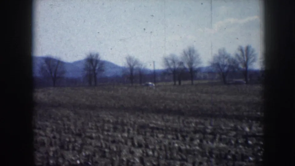 Wide 1958 Nebraska rural view with open ground, bare trees, and low distant hills under a pale sky.