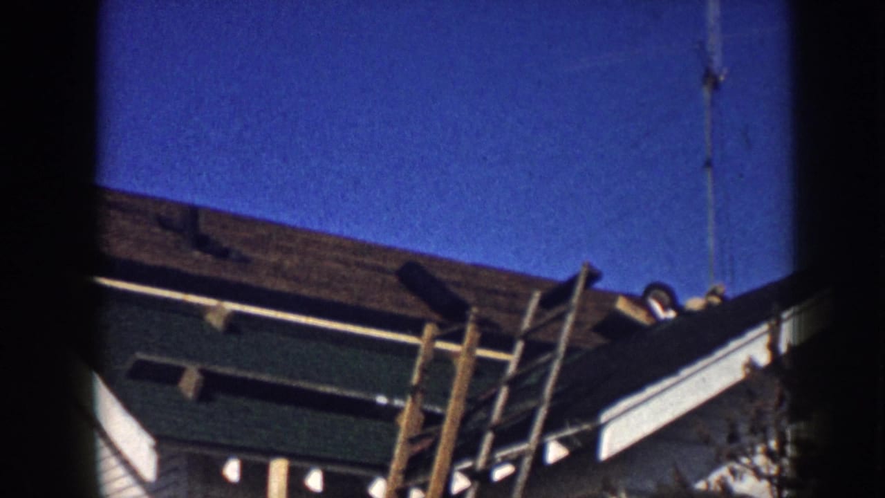 1958 Nebraska home-movie frame showing a house roof, ladder, antenna, and roof edge seen from below.