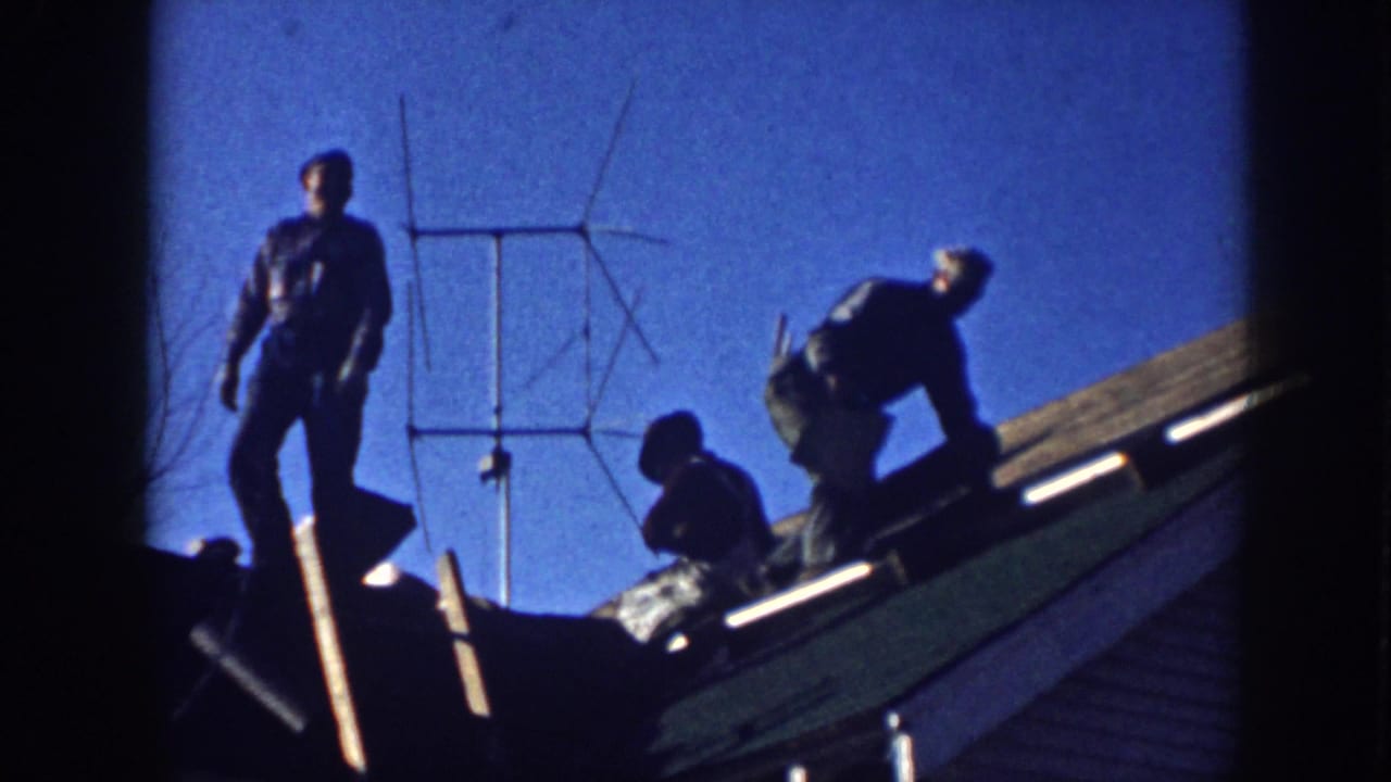 Several men work along a roofline while one stands near a TV antenna.