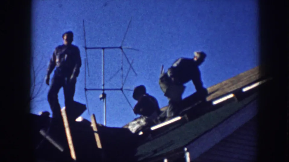 Men on a Nebraska residential roof in 1958, with one figure standing and others bent over near roofing material and an antenna.
