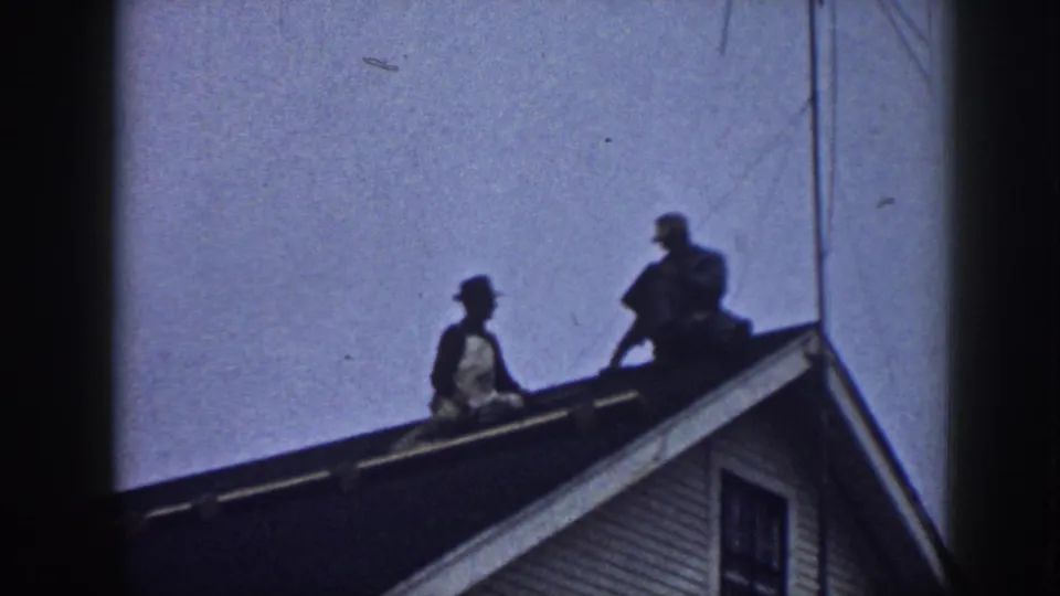 Two figures are visible on the Nebraska house roof, silhouetted against the sky as the repair work continues near the gable end.
