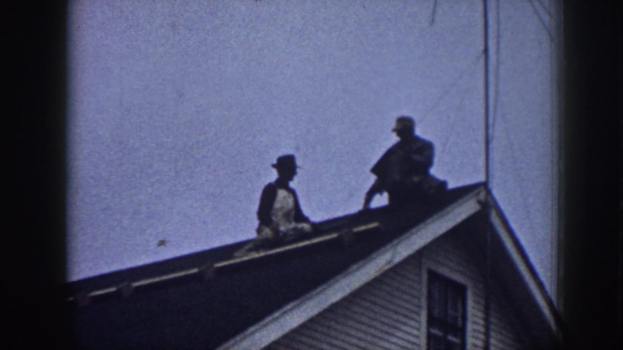 Two men in hats appear on a Nebraska house roof in 1958 home-movie footage, viewed from below against the sky.