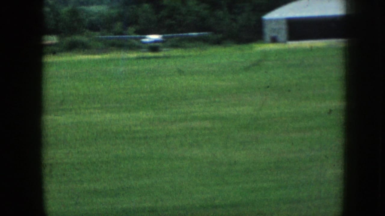 1958 Nebraska 8mm view of a green rural field with distant white structures and trees, seen through dark vertical framing.