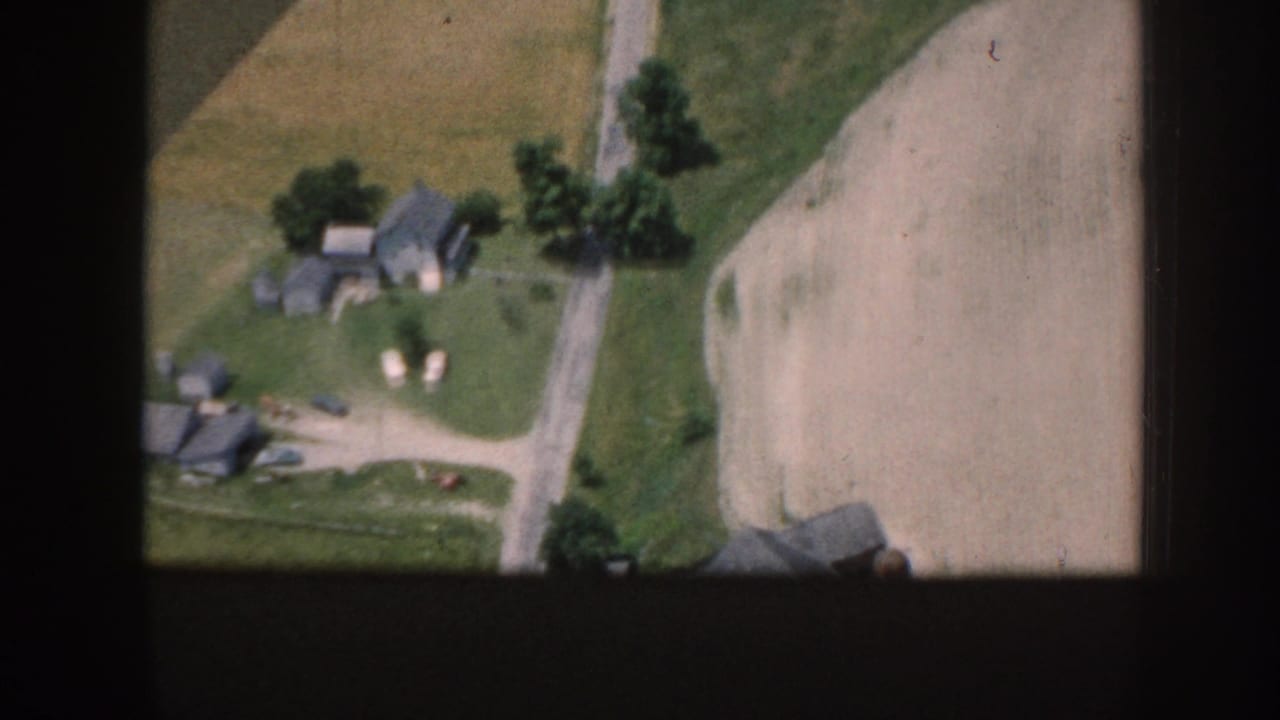 1958 Nebraska aerial frame with scattered farm structures, a road, green grass, trees, and adjacent cultivated fields.