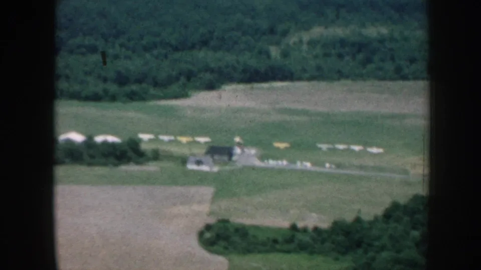 1958 Nebraska aerial frame with fields, wooded edges, a small building cluster, and pale objects arranged across open ground.