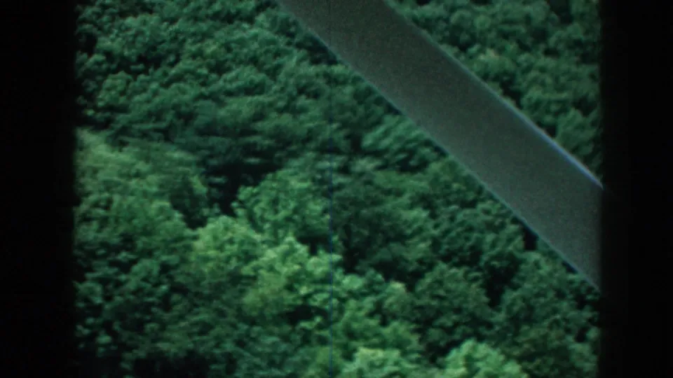 1958 Nebraska 8mm frame looking past an aircraft wing strut toward dense green woods and farmland below.