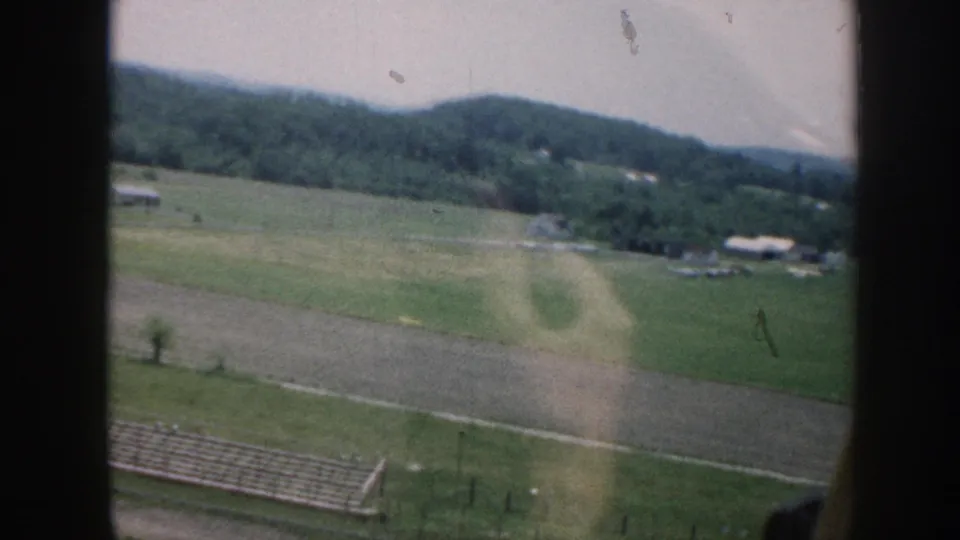 1958 Nebraska airplane-window view showing rural fields, a fenced strip, low hills, scattered buildings, and pale film flare.