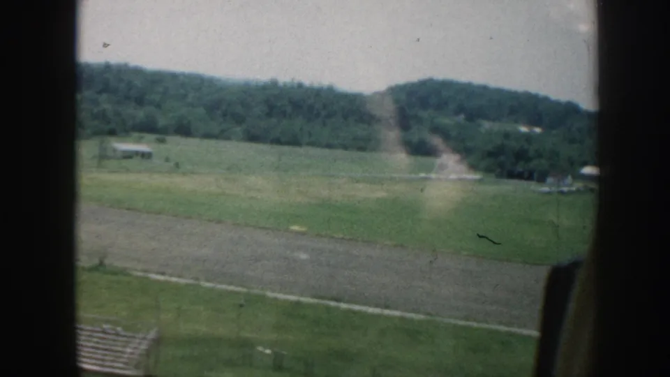 Late-frame 1958 Nebraska aerial view with open fields, wooded hills, fence lines, and the airplane window edge visible.