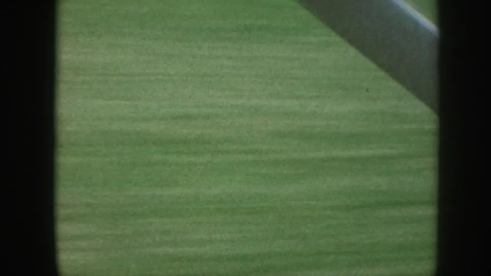 A closer passing view of green grass in Nebraska, partly blocked by dark framing and a diagonal structural bar.