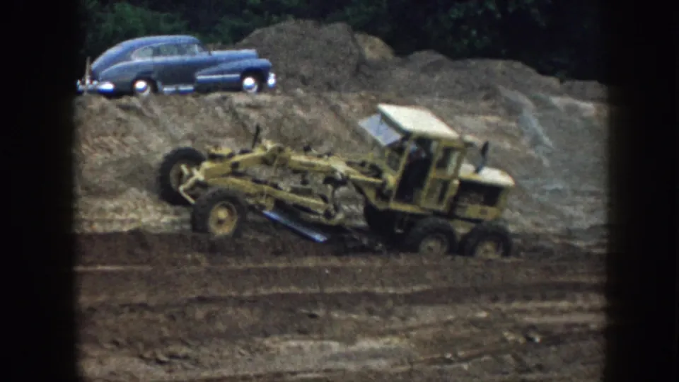 Final 1958 Nebraska frame shows the yellow grader continuing across wet dirt with the blue mid-century sedan above it.