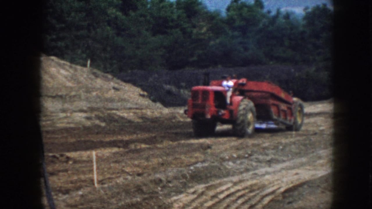 Red tractor-like earthmover moving across a dirt construction area near a soil bank.