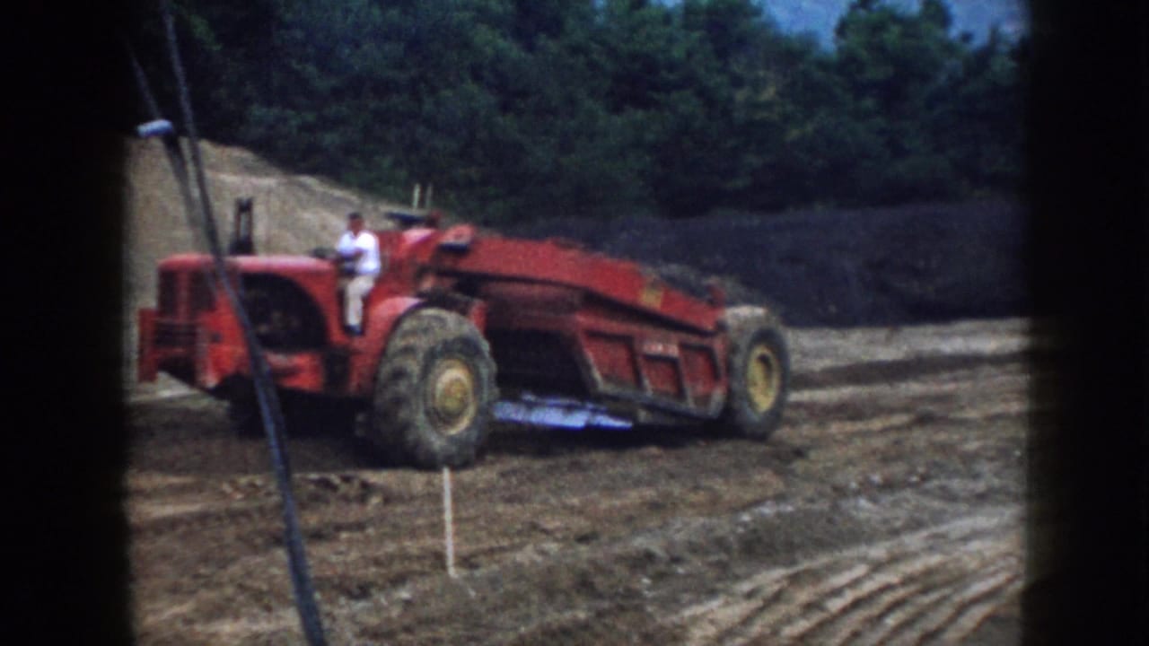 Large red tractor in a Nebraska dirt field, with the operator seated high above the rear wheel in 1958 home-movie footage.