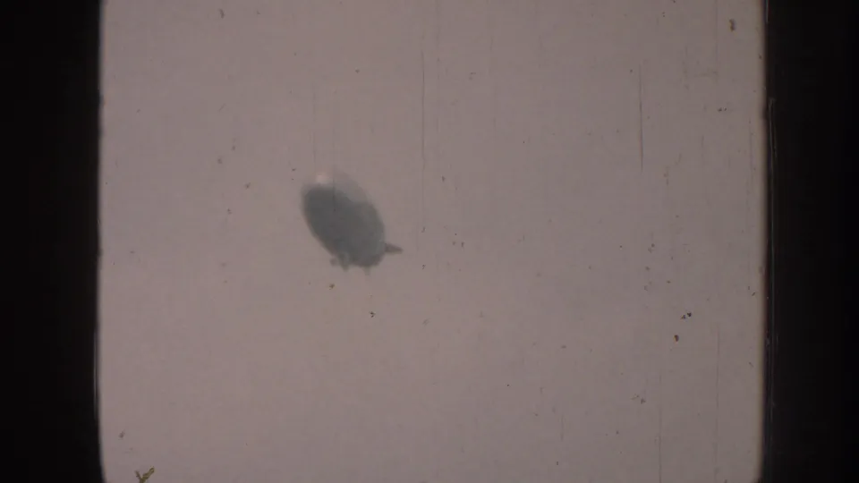 A distant airship-like craft appears as a soft silhouette against a pale sky in 1958 home-movie footage.