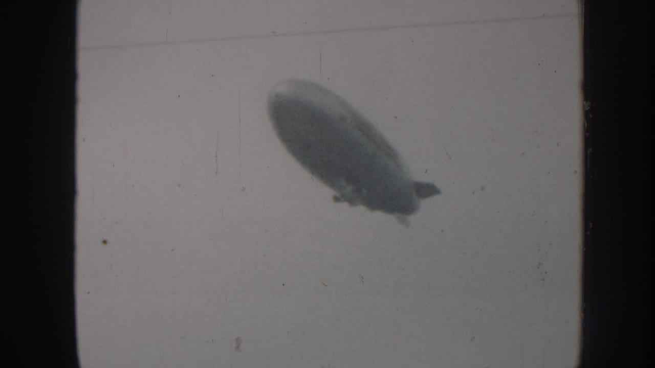 Soft silhouette of an elongated airship against a pale sky.