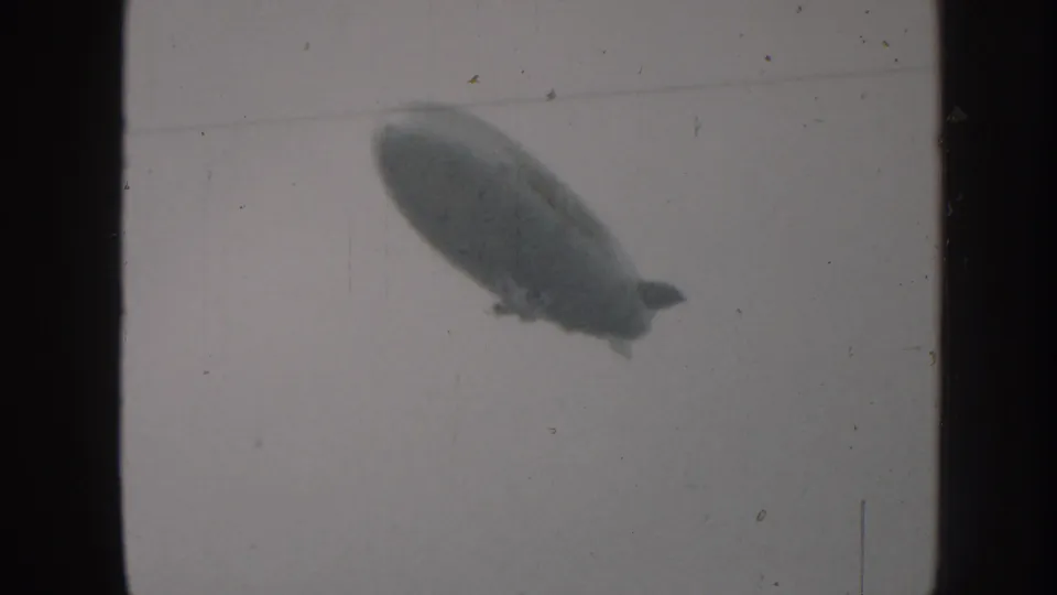 1958 Nebraska 8mm view of the dirigible continuing across the overcast sky, seen as a dark soft-edged form.