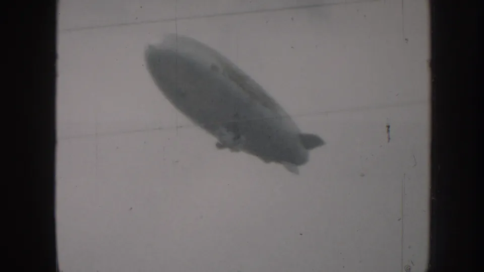 1958 Nebraska 8mm frame showing the dirigible drifting diagonally through a blank, pale sky near the end of the clip.