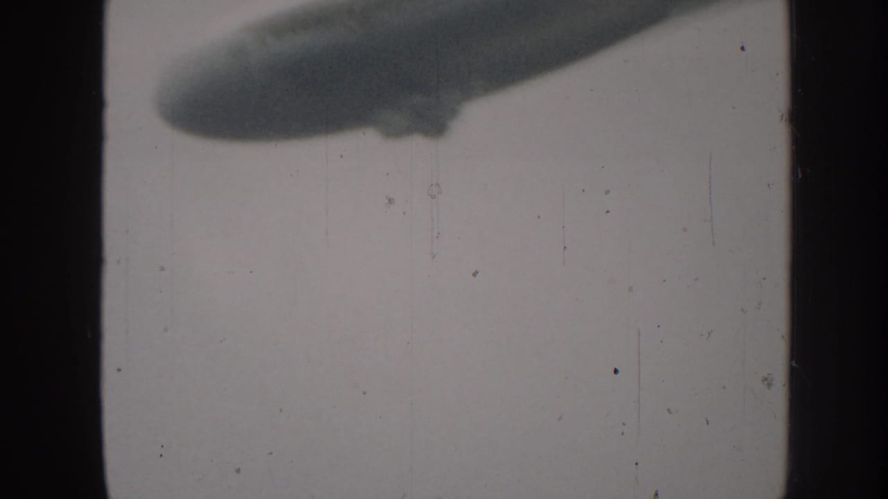 Partial elongated airship silhouette near the top of a cloudy 8mm frame.