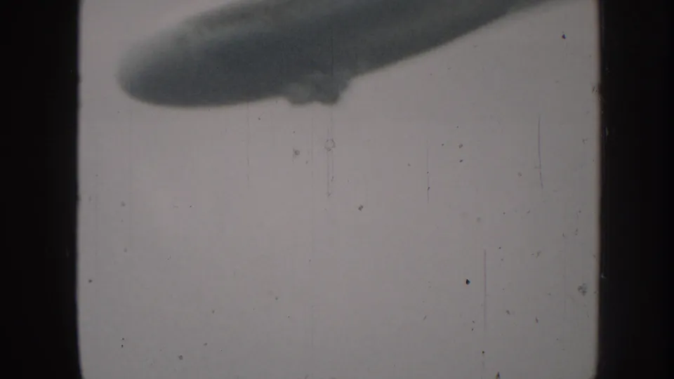 1958 Nebraska 8mm frame showing part of a large airship passing through a pale overcast sky.
