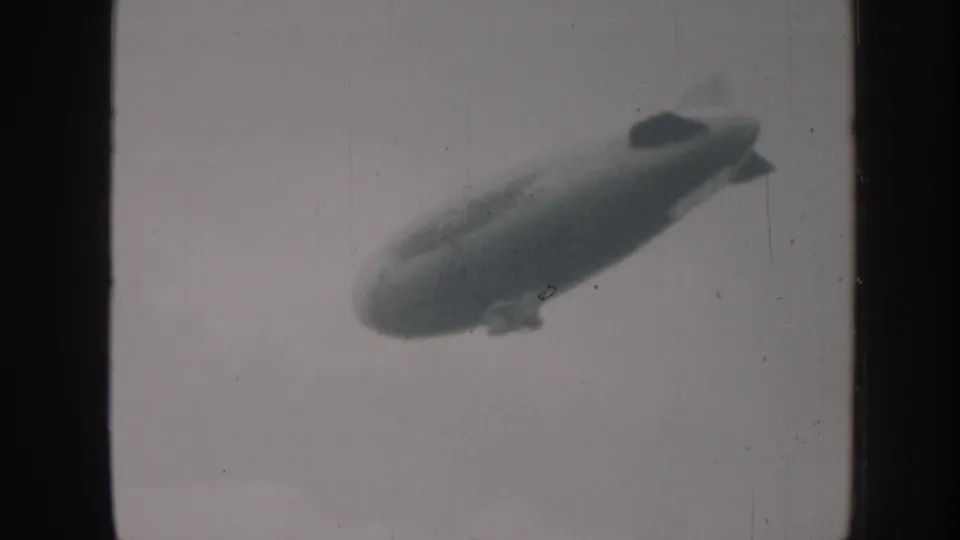 1958 Nebraska 8mm frame with a large blimp-like airship seen from below against an overcast sky.