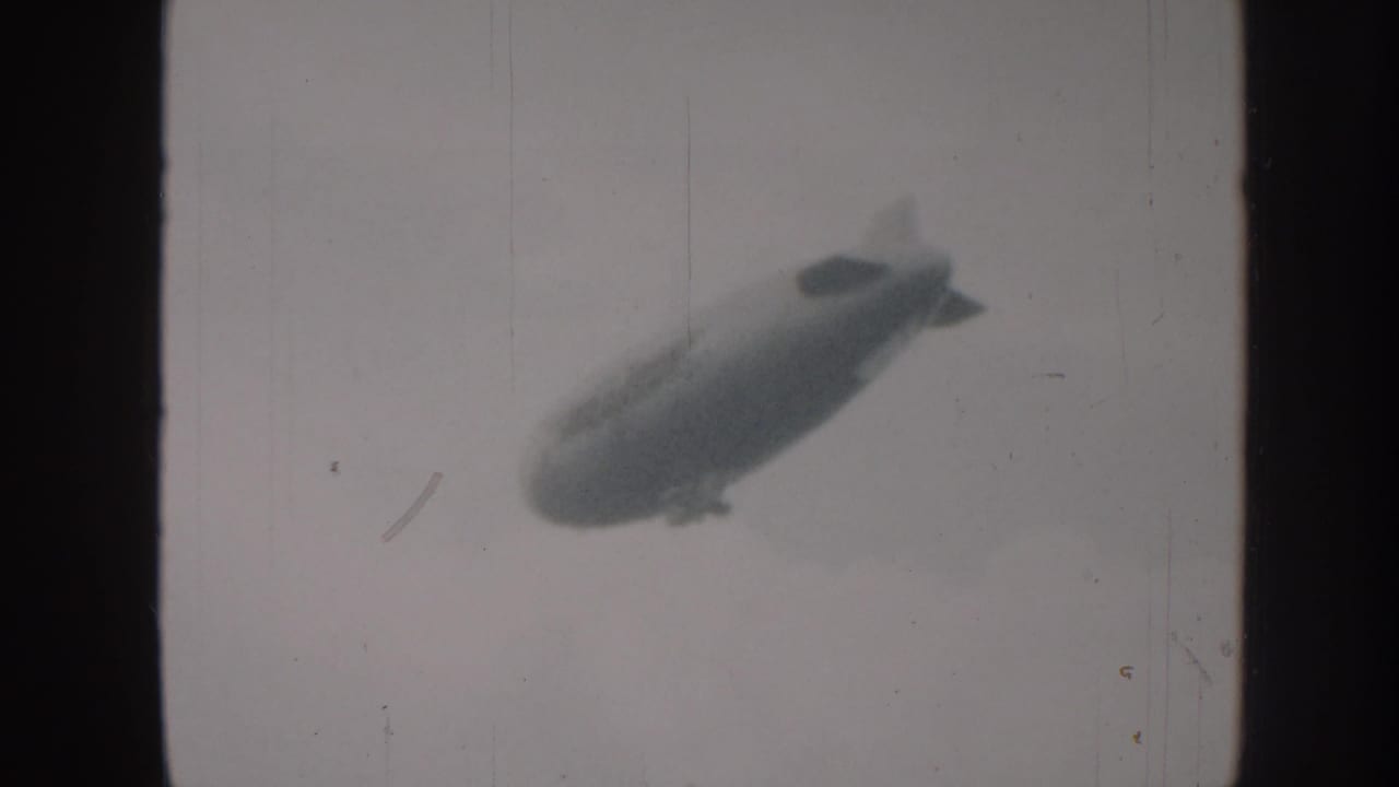 Blimp silhouette in a cloudy sky within an 8mm film frame.